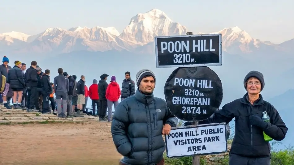 Trekkers posing by the Poon Hill 3210m signpost with a clear view of the snow-capped Dhaulagiri and Annapurna mountain range in Nepal during an Annapurna Base Camp trek.