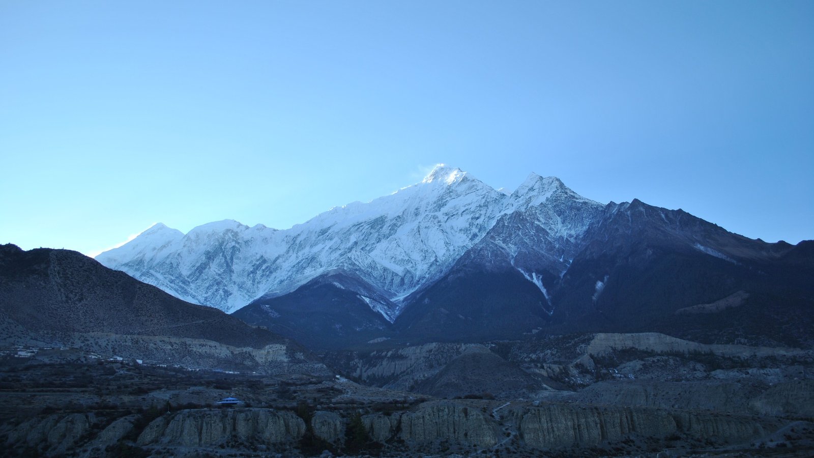 Snow-capped Annapurna mountain range glowing at sunrise, with dramatic ridgelines and rugged terrain in the lower Mustang region of Nepal.