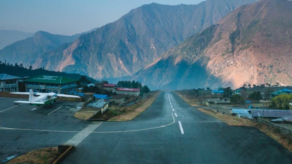 Tenzing-Hillary Airport runway at Lukla, gateway to Everest Base Camp, with mountain backdrop and parked plane at sunrise