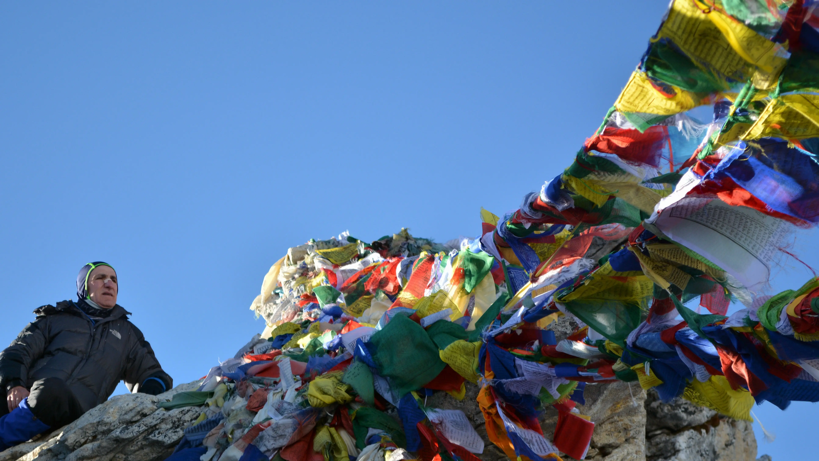 Trekker at Kala Patthar summit with colorful prayer flags and clear blue sky during Everest Base Camp trek