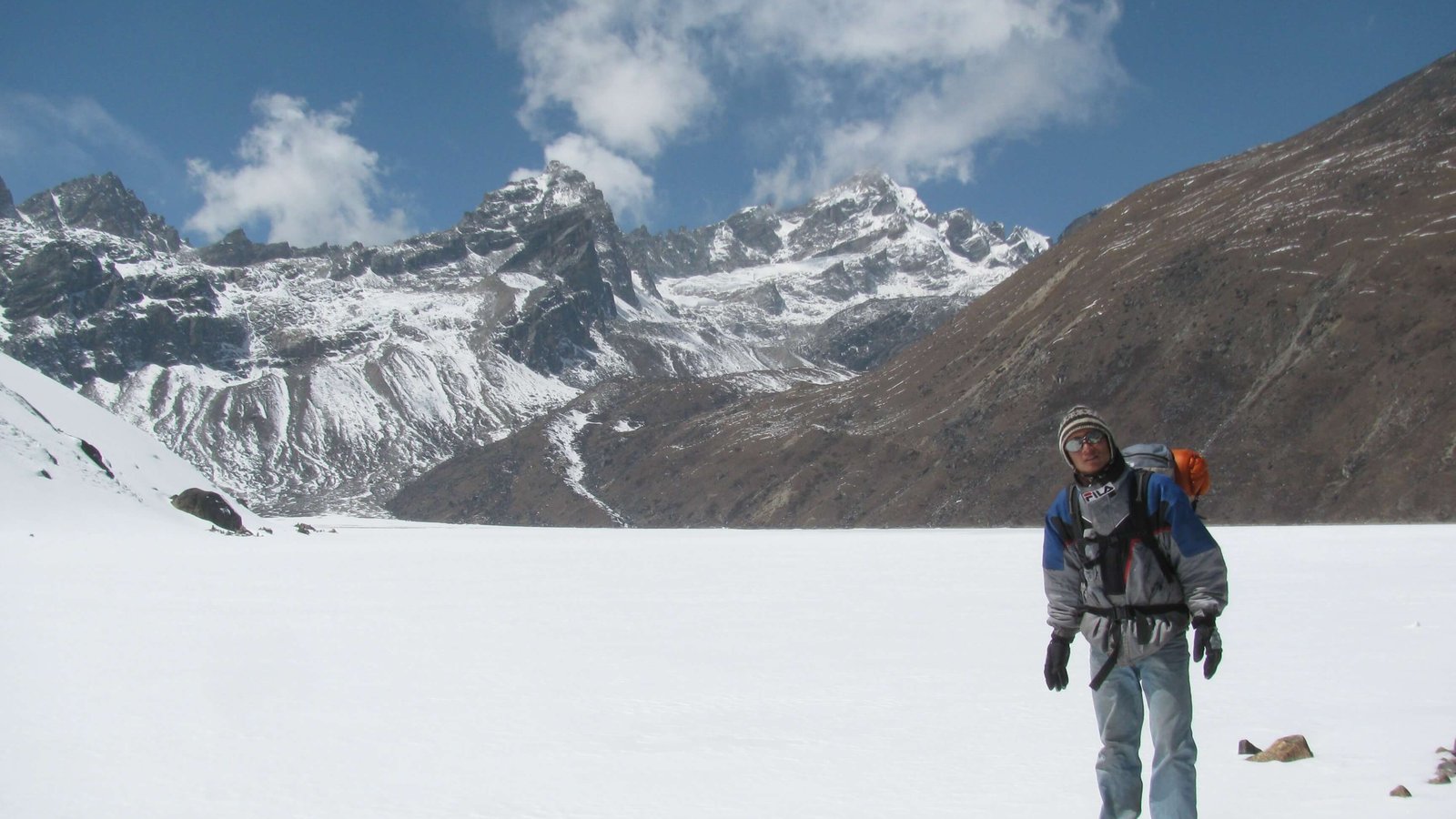 Trekking guide standing near the frozen Gokyo Lake with snowy Himalayan peaks in the background on a clear winter day