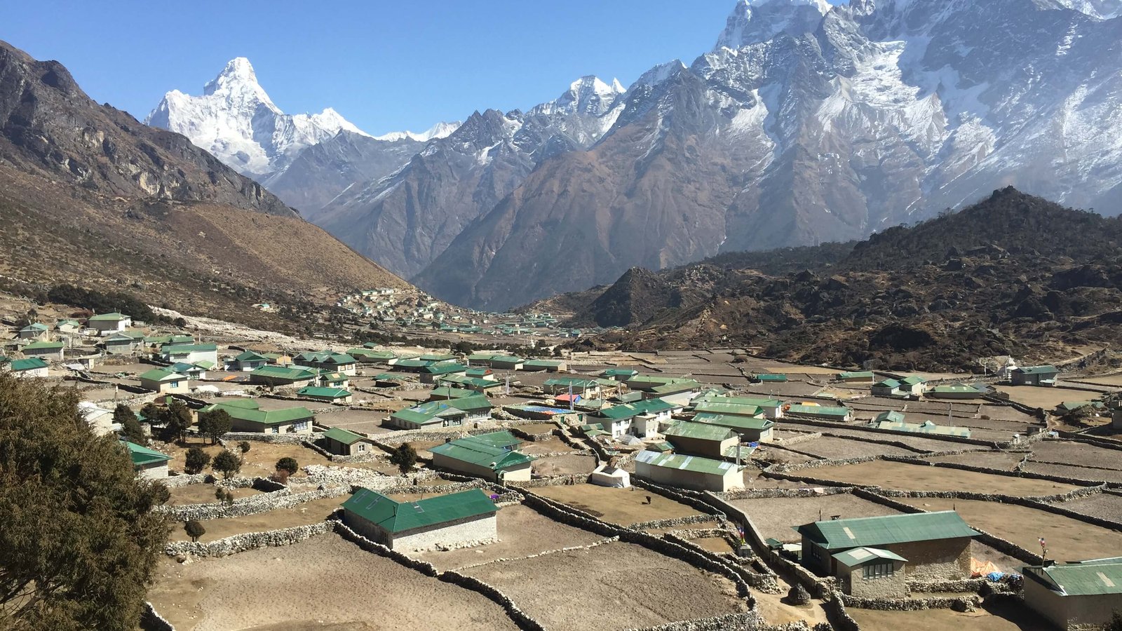 Snow-capped Himalayan peaks surrounding Khumjung village in the Everest Region of Nepal, with rugged terrain and clear blue sky in the background
