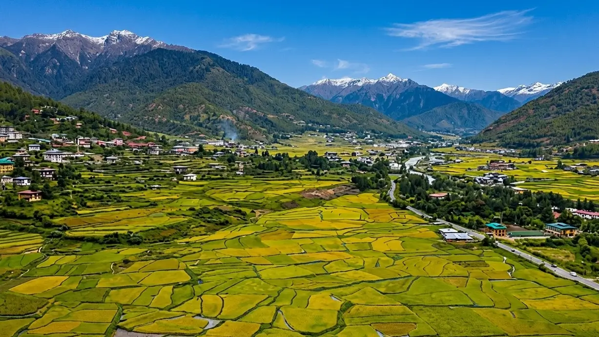 Gaze across the expansive, patchworked floor of the Paro Valley, now revealed in sharp, crystalline clarity. Framed by snow-capped Himalayan peaks and traditional hillside settlements, these ancient terraced fields showcase the timeless harmony of Bhutane