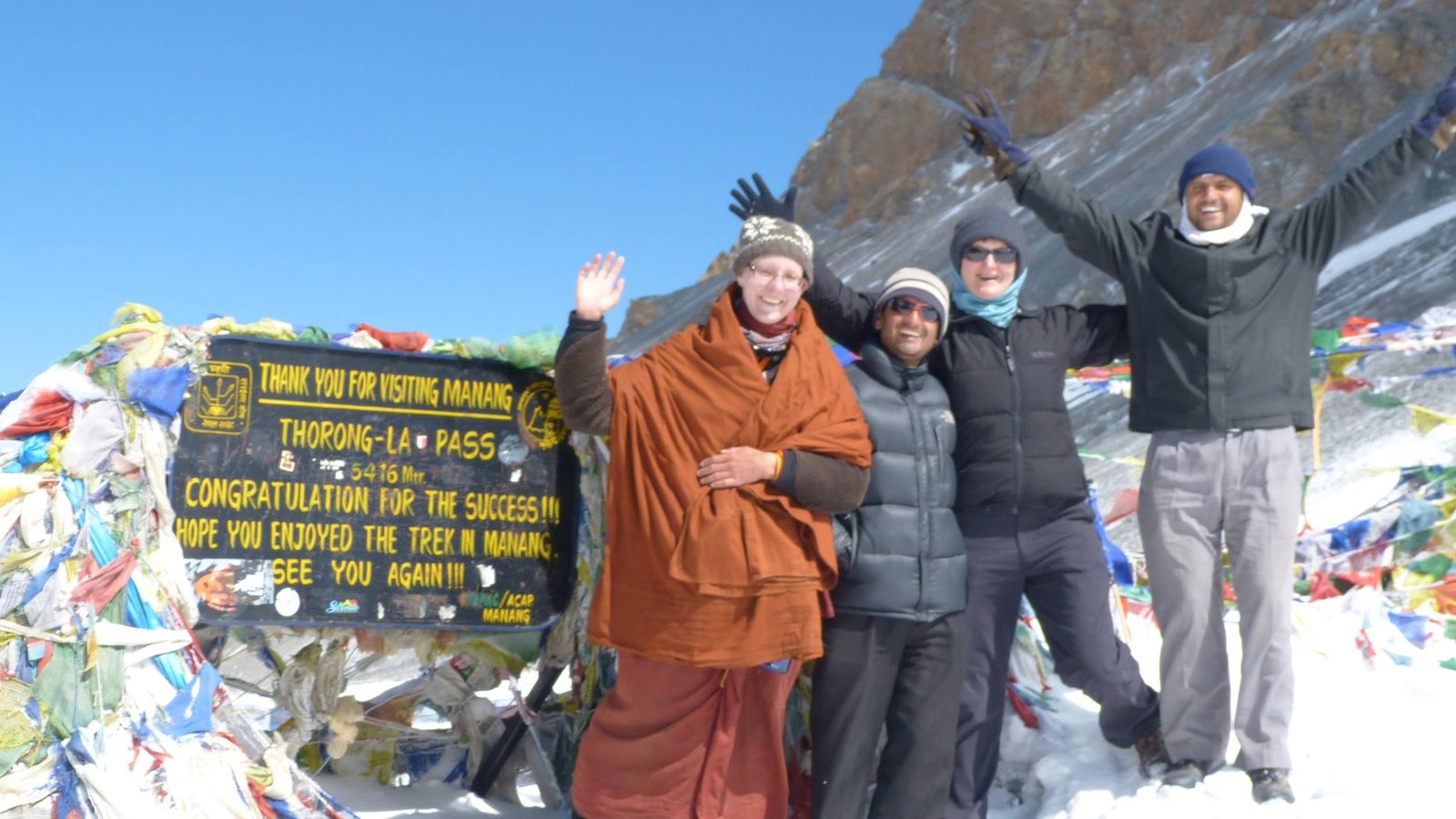 Trekkers standing at the top of Thorong La Pass (5,416m), the highest point of the Annapurna Circuit, with prayer flags and panoramic Himalayan views