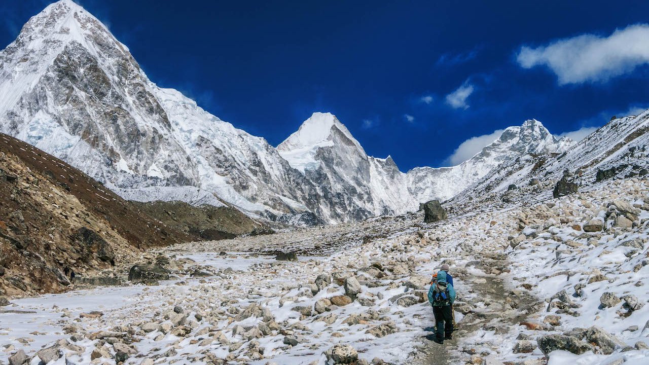 Trekker hiking on snowy trail toward Everest Base Camp with stunning Himalayan peaks and blue sky in the background