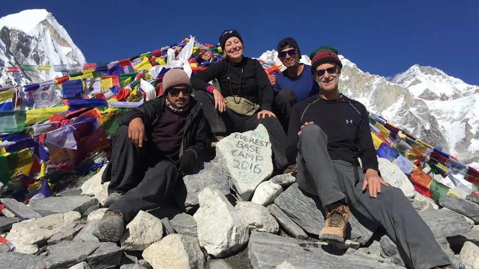Trekkers celebrating at Mount Everest Base Camp with colorful prayer flags in the Himalayas, Nepal